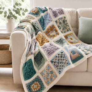Peut inclure: Une couverture en crochet faite à la main composée d'un assemblage de motifs carrés aux textures et motifs variés. La palette de couleurs comprend des tons de bleu sarcelle, vert sauge, lavande douce, jaune moutarde et crème, bordés de crème.