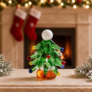 May include: A glass Christmas tree figurine featuring a translucent green body with pointed branches, decorated with small multi-coloured glass spheres in red, blue, yellow, and white. The tree is topped with a white sphere and sits on an amber base.