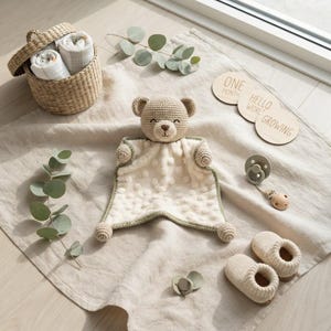 Puede incluir: Una manta de seguridad de oso de ganchillo beige con un cuerpo de tela color crema texturizado, una cesta tejida con dos paños doblados, dos chupetes con clips, un par de patucos de punto y tres discos de madera con las inscripciones One Month, Hello World, Growing.