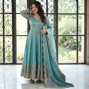 May include: A floor-length, long-sleeved turquoise dress featuring intricate silver embroidery along the hem and neckline. The garment is paired with a matching sheer dupatta that has a scalloped, embroidered edge, creating a cohesive ensemble.