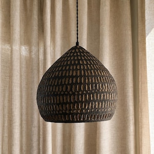 May include: A dome-shaped pendant light fixture with a dark, matte black finish and a textured surface featuring repeating vertical carved indentations. The lamp hangs from a thin, black twisted cord attached to the top center of the dome.