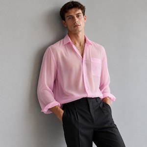 May include: A long-sleeved, semi-sheer light pink button-down shirt with a classic collar, a single chest pocket, and buttoned cuffs, paired with solid black trousers featuring a pleated front and a clean, tailored waistband design.