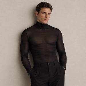 May include: A black long-sleeved turtleneck top crafted from a sheer, semi-transparent material. The garment features a fitted silhouette with a high neck and long sleeves, worn with black trousers that have a visible button closure at the waist.
