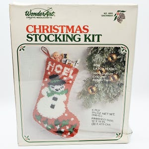 May include: A WonderArt Christmas Stocking Kit for latch hook, featuring a snowman design with the text NOEL. The box includes 100% DuPont Orlon acrylic yarn, 3.75 oz net weight, and states a finished size of 12 by 19 inches, model number 4893.