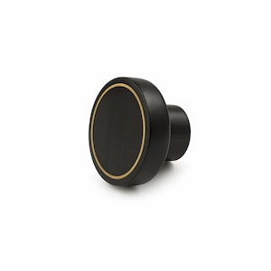 May include: A matte black cabinet knob with a circular silhouette and a thin, recessed gold-toned ring accent on the front face. The hardware features a cylindrical base and a flat, circular front surface, providing a clean and functional design.