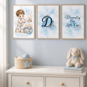Könnte beinhalten: Drei gerahmte Wandbilder mit hellblauem Aquarellmotiv. Das erste zeigt ein Kind mit einem weißen Welpen, das zweite einen großen Buchstaben D mit Blumenakzenten und das dritte den Schriftzug Dream Big Big Little One in blauer Schrift.