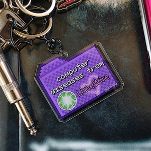 May include: A rectangular acrylic keychain featuring a purple pixelated folder icon with the text "Computer diseases from LimeWire" and a green circular graphic. The keychain is attached to a silver metal split ring and a lobster clasp.