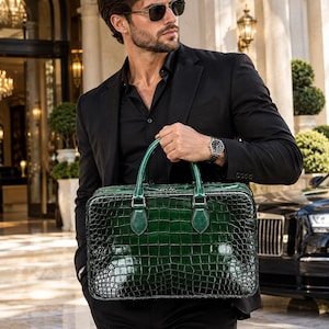 May include: A rectangular briefcase featuring a glossy, dark emerald green finish with a textured, embossed crocodile skin pattern. The bag includes two sturdy top handles, silver-toned hardware, and a secure zippered closure along the top edge.