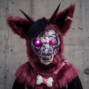 Può includere: Una maschera integrale in pelliccia sintetica color magenta scuro con ciocche di capelli neri e due corna scure appuntite. Il viso ha una texture bianca e nera invecchiata con occhi rosa luminosi e denti bianchi. Un collare rosa con un osso bianco.