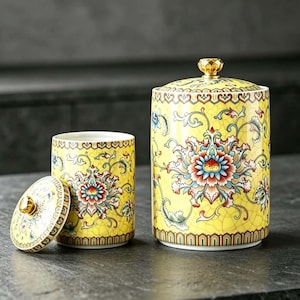 Può includere: Un set di barattoli in ceramica gialla con finitura a smalto crepato e un vivace motivo floreale in rosso, blu e verde. Ogni barattolo ha un coperchio abbinato sormontato da un pomello color oro e il set presenta bordi decorativi complessi.