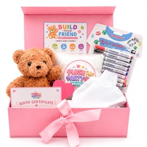 Könnte beinhalten: Eine rosa Geschenkbox mit einem braunen Plüschteddybären, einem weißen T-Shirt, einer Packung Yominmax Textilmarkern, einem Plush Party Boutique Aufkleber, einer Build Your Friend Anleitungskarte, einem rosa Herz und einer Geburtsurkunde.