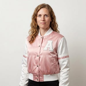 May include: A satin varsity jacket featuring a dusty pink body and white sleeves. The jacket has a white ribbed collar, cuffs, and hem, with a large white letter A patch on the left chest. It includes a front snap button closure and two side pockets.
