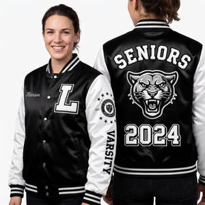 Op de afbeelding: Een zwart-wit varsity jack met een witte letter L op de borst, de naam Harrison en een mouwpatch. De achterkant toont de tekst SENIORS, een afbeelding van een grommende panter en het jaartal 2024 in opvallende witte letters.