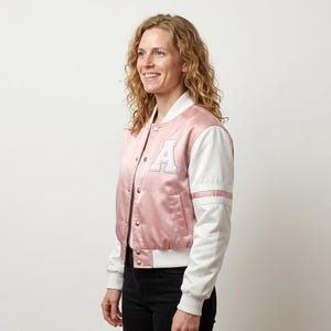 May include: A satin varsity jacket featuring a dusty pink body and white sleeves. The jacket has a white letter A patch on the left chest, a snap button front closure, and white ribbed cuffs and hem. The sleeves include two horizontal white stripes.