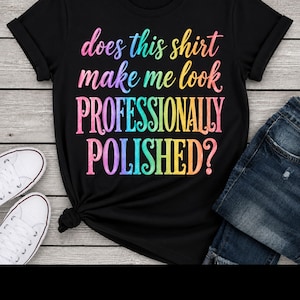 Op de afbeelding: Een zwart t-shirt met korte mouwen en de meerkleurige tekst "does this shirt make me look PROFESSIONALLY POLISHED?" in een regenboogverlooplettertype. Het t-shirt wordt getoond naast witte sneakers en een donkerblauwe spijkerbroek.