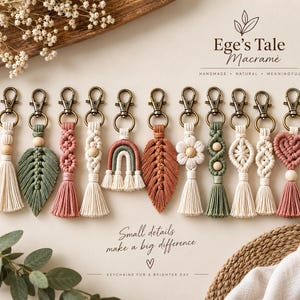 May include: Eleven macrame keychains with bronze-toned lobster clasps, featuring various shapes including leaves, flowers, hearts, and rainbows in cream, sage green, and terracotta colors, with wooden bead accents and tassels, labeled Ege's Tale Macrame.