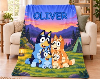 May include: A soft fleece blanket featuring a colourful cartoon scene of four blue and orange dog characters camping in a grassy field at sunset. The name OLIVER is printed in large blue letters at the top above a mountain landscape and a tent.