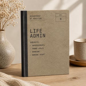 May include: A tan hardcover notebook with a black spine and black text that reads Department of Adulting, Life Admin, and a list of subjects including Appointments, Phone Calls, Banking, and Boring Stuff, with a box labeled Div. E.