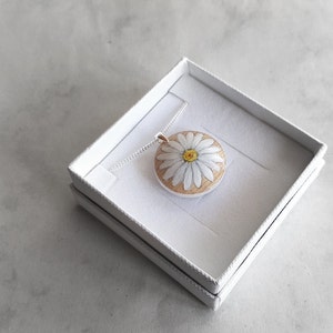 May include: A white daisy flower pendant necklace with a yellow centre, on a silver chain, in a white gift box.