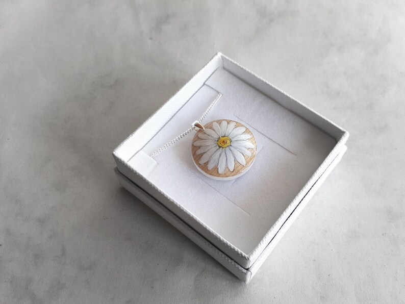May include: A white daisy flower pendant necklace with a yellow centre, on a silver chain, in a white gift box.