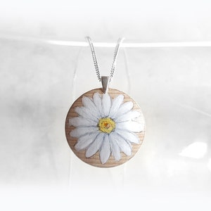 May include: A white daisy painted on a round wooden pendant, hanging from a silver chain.