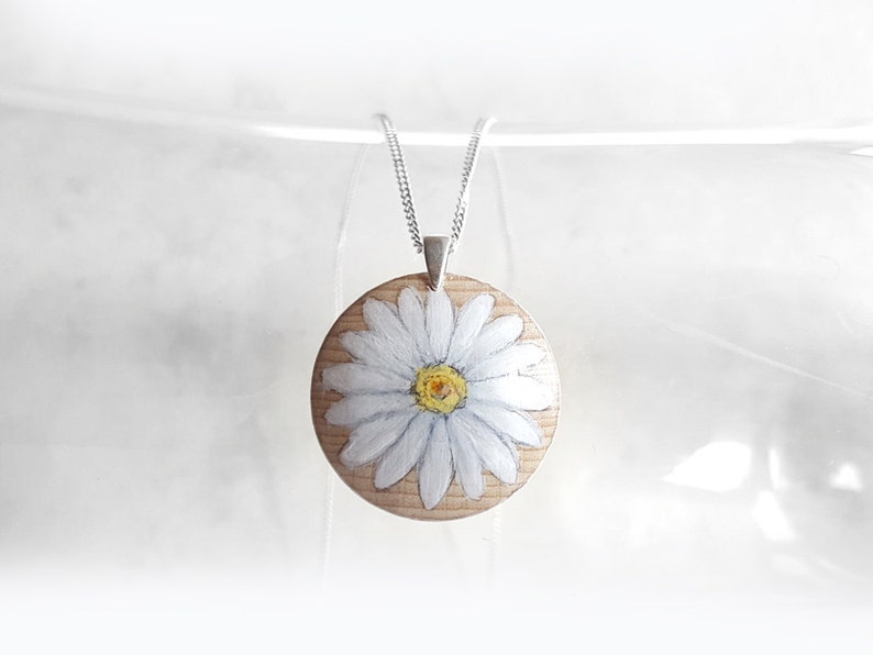 May include: A white daisy painted on a round wooden pendant, hanging from a silver chain.