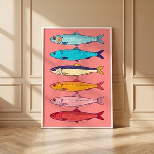 May include: A vertical rectangular wall art print featuring six stylized fish arranged in a column against a solid coral pink background. The fish are rendered in distinct colors including light blue, turquoise, dark blue, yellow, pink, and red.