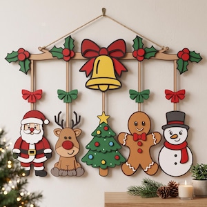 May include: A wooden wall hanging featuring a central yellow bell with a red bow, flanked by five dangling Christmas ornaments: a Santa Claus, a reindeer, a green Christmas tree, a gingerbread man, and a snowman, all accented with small red bows.