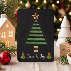 May include: A rectangular black greeting card featuring a stitched green thread Christmas tree design with a gold star topper and a gold trunk. The text Peace & Joy is printed in white, flanked by two small illustrated Christmas trees.