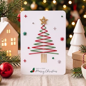 Könnte beinhalten: Eine weiße, rechteckige Grußkarte mit einem Weihnachtsbaum-Design aus abwechselnd rotem und grünem Faden, gekrönt von einem goldenen Stern. Die Karte enthält kleine dekorative Perlen, metallische Akzente und den Text Have a Very Merry Christmas.