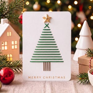 Könnte beinhalten: Eine weiße rechteckige Grußkarte mit einem gestickten Weihnachtsbaum aus grünem Garn. Der Baum ist mit einem goldenen Stern gekrönt und hat einen Stamm aus braunem Garn. Der Text MERRY CHRISTMAS ist unten in Gold aufgedruckt.