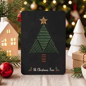 Könnte beinhalten: Eine rechteckige schwarze Grußkarte mit einem gestickten Weihnachtsbaum aus grünem Garn, einer goldenen Sternspitze und einem Stamm aus braunem Garn. Unten steht der weiße Schriftzug "Oh Christmas Tree" neben kleinen Stechpalmen-Symbolen.