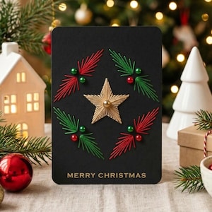 Könnte beinhalten: Eine rechteckige schwarze Grußkarte mit einem zentralen, aus Fäden gefertigten goldenen Stern, umgeben von vier gestickten Zweigen aus rotem und grünem Garn mit kleinen Perlen. Der Text MERRY CHRISTMAS ist unten in Gold aufgedruckt.