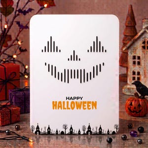 Könnte beinhalten: Eine weiße rechteckige Karte mit einem schwarzen Kürbisgesicht aus vertikalen Linien. Unter dem Gesicht steht der Text "HAPPY HALLOWEEN" in Schwarz und Orange. Der untere Rand zeigt eine schwarze Silhouette einer gruseligen Dorfszene.