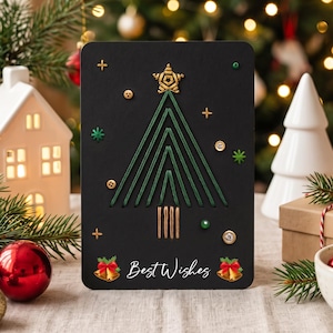 Pode incluir: Um cartão de felicitações retangular preto com um design de árvore de Natal bordado em fio verde e coroado por uma estrela dourada. O cartão inclui botões dourados, pequenas contas verdes e cristais transparentes. O texto Best Wishes está impresso em branco.