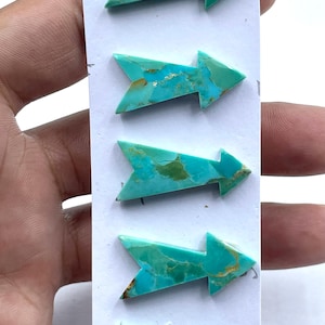 Puede incluir: Cinco cabujones de turquesa en forma de flecha dispuestos verticalmente en una tarjeta de presentación blanca. Cada pieza presenta una vibrante paleta de colores cian y azul verdoso con vetas de matriz marrón natural.