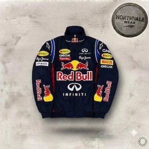 Può includere: Una giacca blu scuro con cerniera caratterizzata da molteplici loghi di sponsor tra cui Red Bull, Infiniti, Geox, Total e Pirelli. La parte anteriore mostra un grande logo Red Bull con due tori rossi contrapposti, insieme al testo Red Bull e Infiniti.