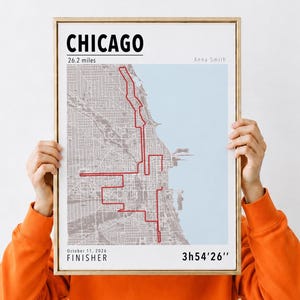 Peut inclure: Une affiche encadrée représentant une carte de Chicago avec un tracé rouge de marathon de 26,2 miles sur un quadrillage gris et de l'eau bleu clair. Le texte indique CHICAGO, Anna Smith, 11 octobre 2026, FINISHER et le temps 3h54'26''.