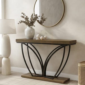 May include: A console table with a rectangular wooden top and base, featuring a black metal frame with curved, petal-like supports. A white ceramic vase with dried eucalyptus branches and three small white spheres sit on the table surface.