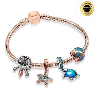 Peut inclure: Un bracelet à maillons serpent en or rose orné de quatre breloques : une pièce ajourée circulaire avec des coquillages pendants, un pendentif étoile de mer texturé, un espaceur serti de cristaux bleus et une perle sphérique en émail bleu.