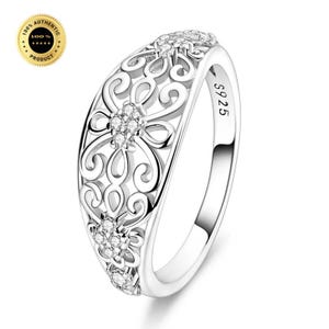 May include: A silver-toned ring featuring an intricate openwork filigree pattern with swirling metal loops and small embedded clear stones. The inner band is clearly stamped with the text S925, indicating the metal composition of the jewelry piece.