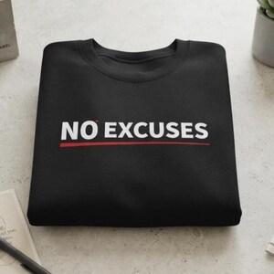 May include: A black crewneck sweatshirt featuring the white text NO EXCUSES printed across the chest. A thin red horizontal line is positioned directly underneath the text, which includes a small red dot above the letter O.