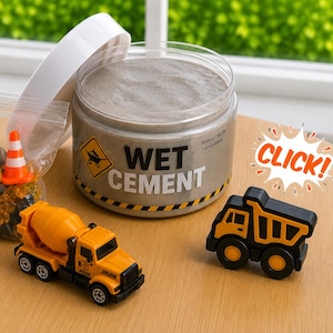 May include: A clear plastic jar labeled WET CEMENT with a white lid, containing gray fluffy slime. Beside it is a plastic bag with two orange traffic cones and small yellow and black stones, plus a yellow cement mixer truck and a black dump truck.