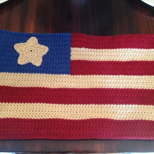 May include: A crocheted American flag placemat with red, white, and blue stripes and a beige star in the blue corner.