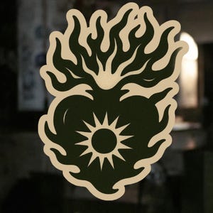 May include: A black and white illustration of a heart with flames around it. The heart has a sun inside of it.