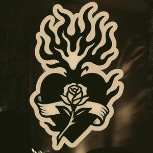 May include: A black and white illustration of a heart with flames on top and a rose in the center. The heart is surrounded by a banner.