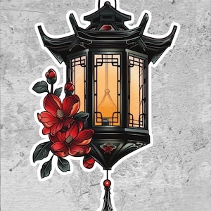 May include: Black pagoda-style lantern sticker with red flowers and green leaves. The lantern has a warm, yellow glow emanating from within. The sticker has a white border and is set against a gray, textured background.