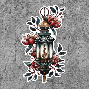 May include: A vintage-style lantern with a blue and gold design, surrounded by pink flowers and green leaves. The lantern has a flame inside and a decorative handle.