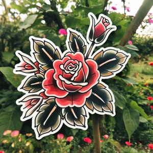 May include: A traditional tattoo style illustration of a red rose with green leaves. The rose is in full bloom and has a delicate white center. The leaves are detailed and have a dark green color.