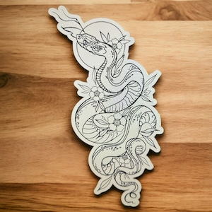 May include: A black and white line drawing of a snake coiled around flowers. The snake is depicted with a detailed pattern and the flowers have simple petals. The drawing is on a white background.